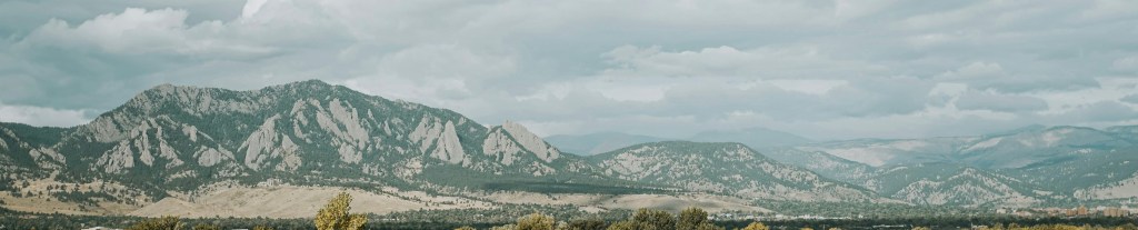 Image of the flatiron mountains overlooking Boulder with clouds in the sky.